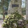 Blick auf ein Denkmal, errichtet aus Anlass steinzeitlicher Funde. Das Denkmal besteht aus mehreren Findlingen, bemoost und unterschiedlich groß, sowie einem aufgesetzten grauen Steinblock. Am Block befindet sich neben einer Tafel ein Geweihstück.