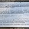 Blick auf eine rechteckige Informationstafel mit viel Text zur Entstehung des Freiburger Schlossbergturmes.