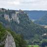 Blick aus großer Höhe auf einen nach links ansteigenden, bewaldeten Berg. An den Hängen des Berges treten graue Felsen hervor. Die Kuppe des Berges ist abgeflacht und teilweise bebaut. Rechts im Hintergrund steht ein weiterer Berg.