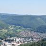 Blick vom Schönbergturm auf eine hügelige bis bergige, stark bewaldete Landschaft. Im Vordergrund, am Fuß der Waldberge, liegen die Ausläufer einer Ortschaft.