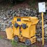 Das Foto zeigt einen alten gelben Wurfschaufellader. Das Arbeitsgerät im Bergbau steht vor einer mit Mauersteinen gesicherten Böschung.