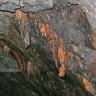 Nahaufnahme von kleinen Tropfsteinbildungen, teils orangerot gefärbt, an einer schrägen Gesteinswand im Besucherbergwerk Hoffnungsstollen bei Todtmoos.