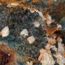 Nahaufnahme von dunkelgrauen Gesteinskristallen, die von weißen und rötlich braunen Gesteinsbildungen durchzogen sind.