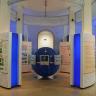 Blick auf den Eingangsbereich Klima und Lebensräume im Staatlichen Museum für Naturkunde Karlsruhe. Im Mittelpunkt steht eine Weltkugel mit verschiedenen Monitoren, links und rechts davon stehen im Halbkreis angeordnete Schautafeln.