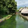 Blick auf einen zum Betrachter fließenden, eingefassten Wasserlauf. Rechts der Einfassung stehen Gebäude, am linken Ufer Bäume und Gebüsch.