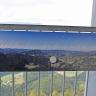 Blick auf ein in großer Höhe befindliches Metallgeländer eines Aussichtsturmes. Am Geländer ist ein Panormabild mit den umgebenden Bergen und Ortschaften angebracht.