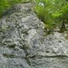 Das Bild zeigt eine größere, freiliegende Felswand. Das Gestein ist grau mit leichten Schattierungen. Unten und oben verlaufen waagrechte Einkerbungen, in der Mitte führen sie senkrecht hinauf. An den Seiten wachsen Bäume.
