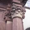 Aufwärts gerichteter Blick auf eine Säule sowie Kapitelle aus rötlich grauem Gestein an einer Kirchenfassade.