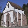 Das Foto zeigt den Gebäuderest einer Kirche oder eines Klosters. Der schmale weiße Bau wird von rötlichen Strebepfeilern gestützt. Der Eingangsbereich ist ebenfalls mit rötlichen Steinen umsäumt.