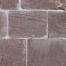 Nahaufnahme von rötlich grauem Mauerwerk mit schmalen hellen Fugen. Die Mauersteine sind rechteckig und weisen dünne Furchen auf.