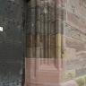 Seitenansicht eines Toreingangs aus rötlichem, am Tor schwärzlichem Mauerwerk. Auffallend ist ein neu eingesetztes Sockelstück aus rosafarbenem Gestein.