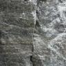 Nahaufnahme von dunkelgrauem Gestein mit senkrecht verlaufendem Riss in der Mitte und weißlichen Kristallen rechts. Links ist ein Maßstab angebracht.