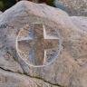 Nahaufnahme eines graurosa Grabsteines mit stilisiertem, aus dem Stein gemeißelten Kreuz.