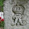 Die Aufnahme zeigt einen grauen Grabstein mit herausgearbeitetem Wappen (unter anderem eine Krone).