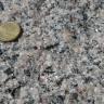 Nahaufnahme einer kristallinen Gesteinsoberfläche, Farbe grau mit bräunlichen Stellen. Links oben liegt eine 10-Cent Münze. 