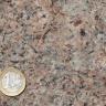 Nahaufnahme einer rötlich grauen Gesteinsoberfläche. Links unten liegt eine Euro-Münze.