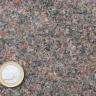 Nahaufnahme einer dunkelgrauen bis rötlich grauen Gesteinsoberfläche. Links unten liegt eine Euro-Münze.