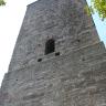 Teilansicht eines hohen Burgturms aus rötlich grauen Mauersteinen. In der Bildmitte ist eine Fensteröffnung im Turm eingelassen.