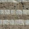 Nahaufnahme einer Steinmauer, wechselagig gesetzt aus zwei unterschiedlichen Materialien: weißliche schraffierte Blöcke, quadratisch bis rechteckig, sowie größere und kleinere graue Blöcke mit löchriger Oberfläche.