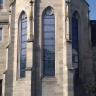 Blick auf einen mehreckigen Kirchenbau aus grünlich grauem Mauerwerk mit Stützpfeilern und Fenstern mit Spitzbogen.