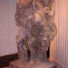 Blick auf eine ausgestellte Bildhauerarbeit aus römischer Zeit. Material rötlich graues Gestein, mit ausgebleichten und verwitterten Stellen. Die Figur soll Herkules darstellen, ihr fehlt allerdings der Kopf.