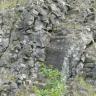 Auf diesem Bild liegen an einem Hang abwärts graue bis dunkelgraue Steinbrocken bogenförmig aufeinander und bilden dabei fast eine Art Rutschbahn.