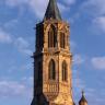 Blick auf einen gotischen Kirchturm aus rötlichem Mauerwerk, von der Abendsonne angestrahlt.