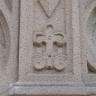 Teilansicht einer Kirchenfassade aus hellgrauem, fleckigem Stein mit herausgearbeitetem Ornament in Form einer Kreuzblume.