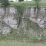 Blick auf zwei hellgraue Gesteinswände, die an einem teils zugewachsenen Hang hervortreten. Teile des Gesteins sind abgerutscht und haben kaminartige Schlote gebildet.