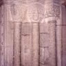 Teilansicht eines Kirchenportals mit drei schmalen Säulen und verzierten Aufsätzen aus rötlich grauem Stein.