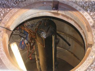 Blick auf den Sondenkopf mit inliegendem Wärmetauscher einer Phasenwechselsonde (Foto: Stober & Bucher, 2014) Das Bild zeigt ein in einen Erdschacht hinabgelassenes, zylindrisches Gerät mit angeschlossenen Kupferrohren und Kabeln.