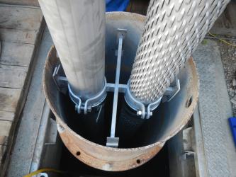 Die Ruhetemperaturprofilmessungen erfolgen u. a. durch stationär in die Erdwärmesonden eingebaute Glasfaserkabel Das Foto zeigt ein verrohrtes Bohrloch mit zwei herausragenden Metallrohren, mit denen durch pumpen der Grundwasserspiegel abgesenkt wird.