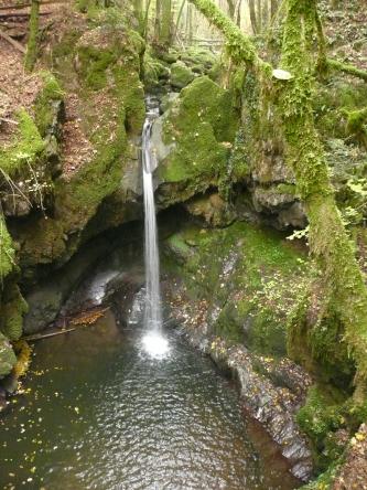 Oberer Haselbach-Wasserfall bei Indlekofen, Waldshut-Tiengen Blick aus großer Höhe auf einen schmalen Wasserfall, der sich über stark bemooste Felsformationen in die Tiefe stürzt.