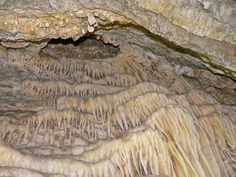 Blick auf wellenförmig angeordnete Tropfsteinbildungen in einer Höhle. Am oberen Bildrand verläuft ein Gesteinsvorsprung ähnlich einem Dach..