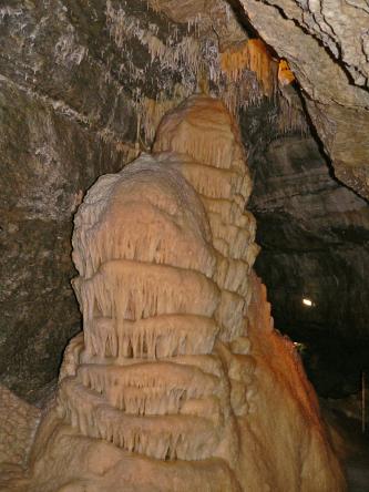 Blick auf einen mehrstöckigen, von unten nach oben gewachsenen Tropfstein in einer Höhle. Der schöne Stalagmit hat eine rosa Oberflächenfärbung. 