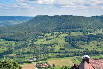 Der Albtrauf am Breitenstein bei Ochsenwang – Hinten links der Erkenberg bei Neidlingen Blick von einem Aussichtspunkt auf einen bewaldeten, oben abgeflachten Berg. Am gewölbten Berghang wechseln sich Wiesen und Bäume ab, am Fuß des Berges folgen flache Äcker.