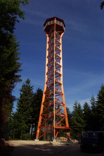 Auf einer kleinen Waldlichtung steht ein von hölzernen Strebepfeilern gestützter Aussichtsturm. In der Turmmitte verläuft eine Aufstiegstreppe. Oben ist eine überdachte Kanzel angebracht.