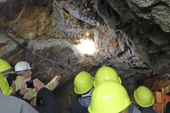 Blick in ein ehemaliges Bergwerk während einer Führung. Der Führungsleiter erhellt die niedrigen Deckenwände mit einer Taschenlampe.