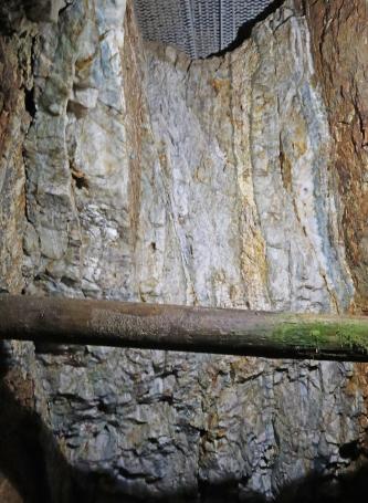 Teilansicht einer Abbauwand in einem ehemaligen Bergwerk. Das sichtbare Gestein ist violettgrau, mit senkrecht verlaufenden gelblichen Streifen.