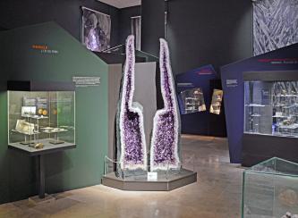 Große Amethyst-Druse in der Mineralienabteilung des Staatlichen Museums für Naturkunde Karlsruhe Blick in die Mineralienabteilung des Naturkundemuseums in Karlsruhe. Zwischen mehreren Schaukästen mit Mineralienfunden steht auf einem Sockel ein großer Amethyst, der in zwei Hälften aufgeschnitten wurde, um das Innere zu zeigen.