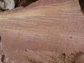 Das Bild zeigt einen größeren Gesteinsbrocken, auf dessen Oberfläche helle, gelbliche Streifen das sonst vorherrschende Rosa unterbrechen.