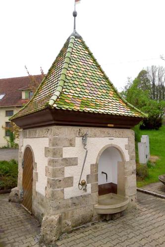 Der Mineralwassersäuerling von Kleinengstingen wurde in einem 4,5 Meter tiefen Schachtbrunnen gefasst und mit einem Brunnenhäuschen überbaut Blick auf ein gemauertes Brunnenhäuschen mit pyramidenförmigem Dach. Rechts ist eine Öffnung im Gebäude, dort ragt das steinerne Brunnenbecken heraus.
