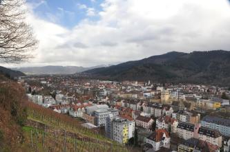 Weiter Blick auf einen Stadtteil von Freiburg. Die im Dreisamtal liegenden Bezirke erstrecken sich zwischen Weinberghängen rechts und bewaldeten Bergen links sowie im Hintergrund.