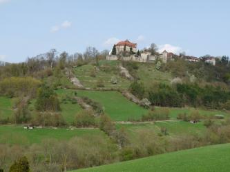 Auf der Kuppe eines nach oben hin steil ansteigenden grünen Hanges thront Schloss Stetten. Im oberen Bereich des Hanges sind sowohl längs- als auch abwärtslaufende Steinhügel zu erkennen. Auch Baum- und Waldstreifen durchziehen den Hang.