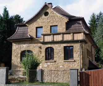Dieses Bild zeigt ein aus gelblich braunen Steinen erbautes Haus mit dunklem, stufigem Dach. 