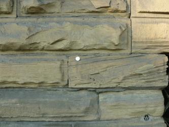Das Bild zeigt mehrere, waagrecht aufeinanderliegende Mauersteine. Die Steine sind grünlich blau und weisen feine Furchen auf.