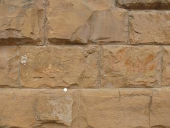 Blick auf drei Stufen einer gelblich braunen bis rötlichen Steinmauer mit senkrechten und waagrechten Einkerbungen.