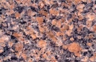 Detailaufnahme einer polierten Steinplatte. Das Gestein hat große, orange-rosane Kristalle, hellgraue Kristalle, weißliche Kristalle und schwarze, kleine Kristalle. Der Bildausschnitt hat eine Breite von 12 cm.