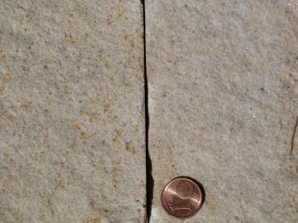 Nahaufnahme zweier durch einen senkrecht verlaufenden Spalt getrennten, bräunlich grauer Steinplatten. Eine unten rechts liegende Centmünze dient als Größenvergleich.