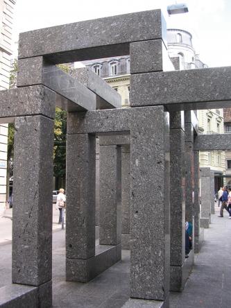 Das Foto zeigt mehrere vierkantige graue Steinsäulen, die – kunstvoll zusammengefügt – verschiedene begehbare Durchgänge, aber auch Sitzgelegenheiten bieten.